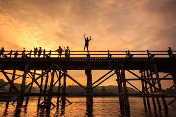 Fototapeta na wymiar The silhouette young boy jumping of old wooden bridge Bridge collapse Bridge across the river and Wood bridge (Mon bridge )at sangklaburi, kanchanaburi