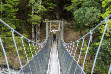 young adult woman passes the river on a suspension bridge on the