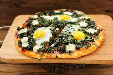 Round green pizza with eggs and mozarella on wooden board