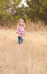 Cute kid girl walking in meadow. Looking at camera. Childhood. 