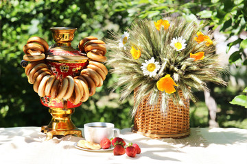 A cup of morning tea on table with samovar and beautiful bouquet of summer flowers on nature background