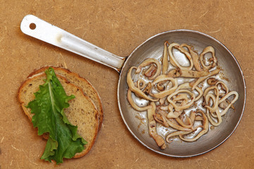 Roasted squids pieces in frying pan and bread slices.Top view.