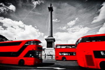Red buses in motion on Trafalgar Square in London, UK. Nelson's column