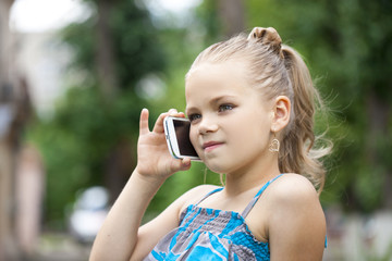 Little girl talking on cell phone against green of Park in summe