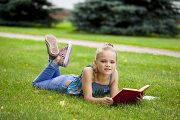 Adorable cute little girl reading book outside on grass