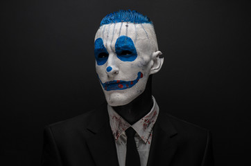 Terrible clown and Halloween theme: Crazy blue clown in black suit isolated on a dark background in the studio