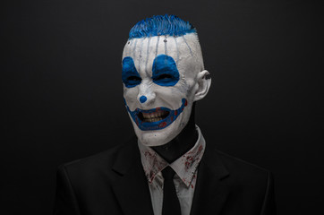 Terrible clown and Halloween theme: Crazy blue clown in black suit isolated on a dark background in the studio