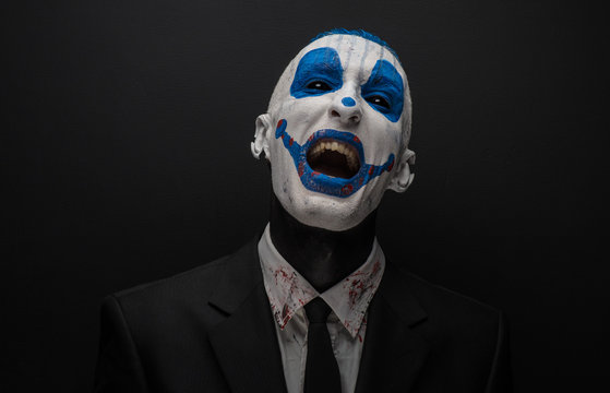 Terrible clown and Halloween theme: Crazy blue clown in black suit isolated on a dark background in the studio