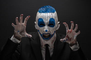 Terrible clown and Halloween theme: Crazy blue clown in black suit isolated on a dark background in the studio