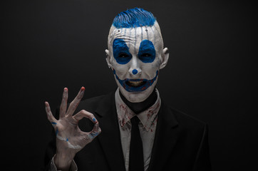 Terrible clown and Halloween theme: Crazy blue clown in black suit isolated on a dark background in the studio