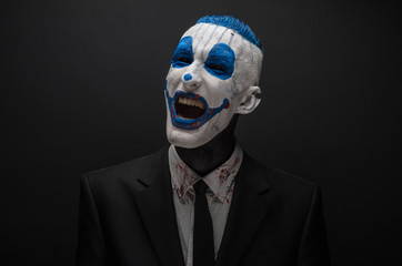 Terrible clown and Halloween theme: Crazy blue clown in black suit isolated on a dark background in the studio