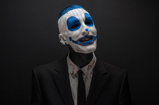 Terrible clown and Halloween theme: Crazy blue clown in black suit isolated on a dark background in the studio