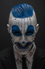 Terrible clown and Halloween theme: Crazy blue clown in black suit isolated on a dark background in the studio