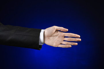 Businessman and gesture topic: a man in a black suit and white shirt showing hand gesture on an isolated dark blue background in studio