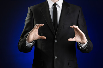 Businessman and gesture topic: a man in a black suit and white shirt showing gestures with hands on a dark blue background in studio isolated