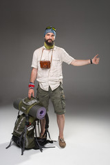 Male tourist with backpack hitchhiking on gray background