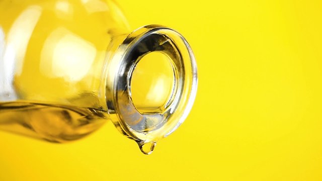 pouring olive oil with the bottle on yellow background, concept of diet and nutrition 