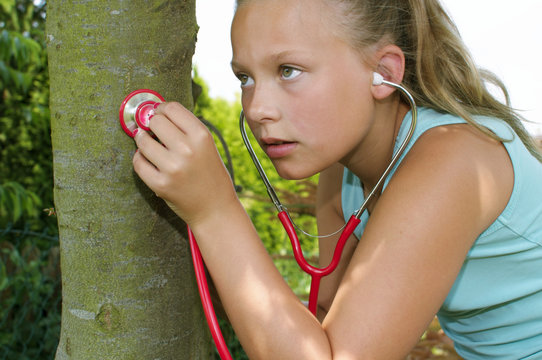 Mädchen lauscht mit einem Stethoskop an einem Baum.