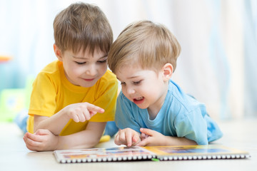 Kids brothers practice reading together looking at book laying on the floor