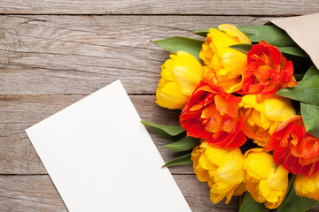 Colorful tulips and greeting card on wooden table