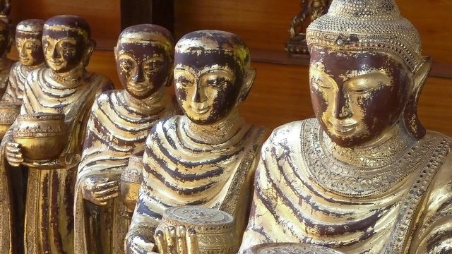 Row of handcrafted ceramic Buddha statues depicting a smiling Buddha as a monk with a begging bowl, closeup view in an oblique receding line