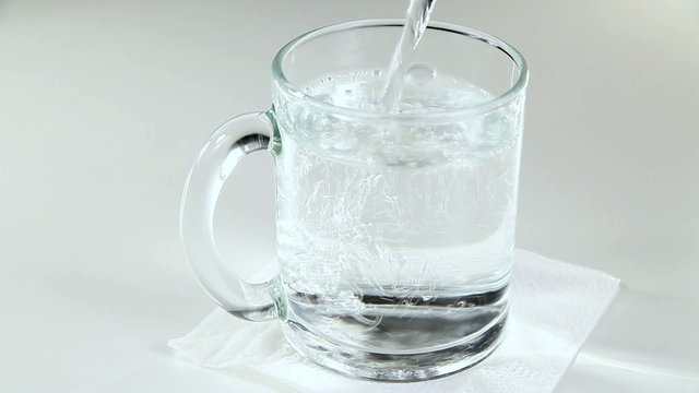 Mineral Water is Poured Into a Glass Mug on a White Background