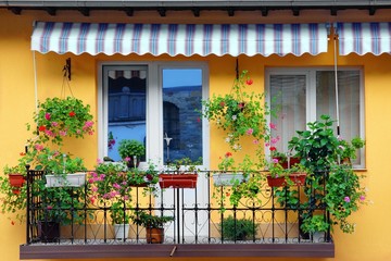 Yellow Building Wall With Balcony Flowery Garden - obrazy, fototapety, plakaty