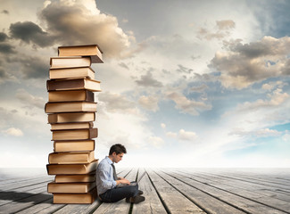 Column of books and young man with laptop
