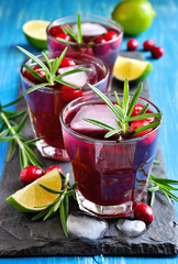 Red refreshing cranberry cocktail with rosemary, lime, and ice cubes, selective focus