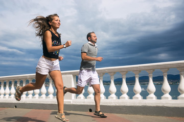 Young sports couple runs along the promenade by the sea