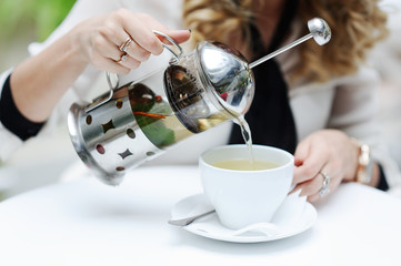 woman pours green tea from teapot into a cup
