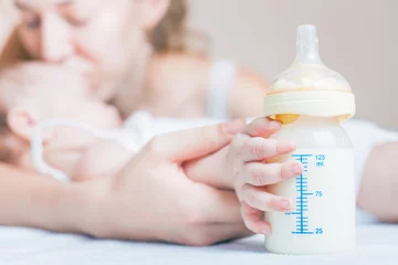Baby hält eine Babyflasche mit Muttermilch zum Stillen. Muttermilch ist die gesündeste Nahrung für Neugeborene. © petunyia