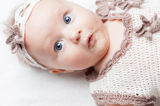 happy baby girl dressed in knitted pretty costume, lies on a white background and looking up. There is concept or idea of love, family and happiness at the home