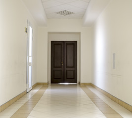 White hallway with marble floor and brown door in hospital