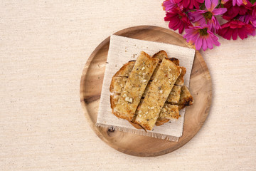 Garlic bread on wooden plate with flower on background