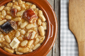 Spanish fabada in an earthenware dish and a wooden spoon