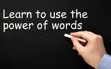 Male hand wearing a business shirt writing the phrase Learn to use the Power of Words in white text on a blackboard