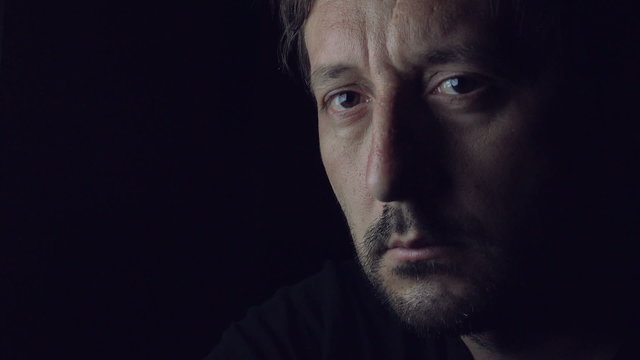 Sad Adult Caucasian Man Sitting Alone in Dark Room Late at Night with TV Light Flickering