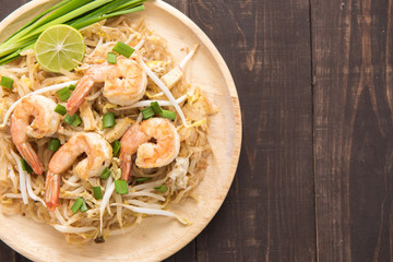 Asian rice noodles with shrimp and vegetables on wooden table.