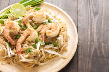 Asian rice noodles with shrimp and vegetables on wooden table.