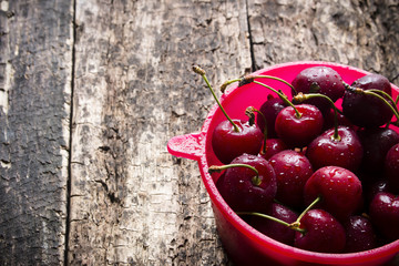 Rural berry cherry with drops of water in a red bucket on a wooden table