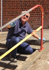 A painter painting handrails along a walkway with concrete steps