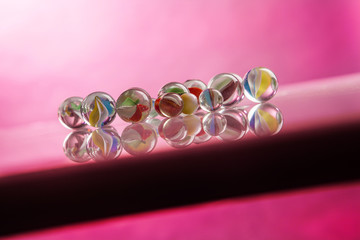 Biglie di vetro colorato su piano obliquo, con sfondo fucsia