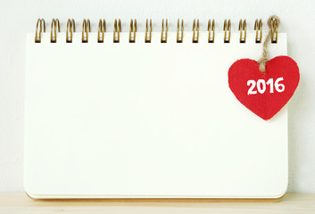 Red fabric heart with 2016 word hanging on blank note book, new year template