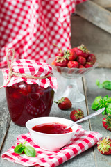 Confiture with strawberries and basil on a wooden background