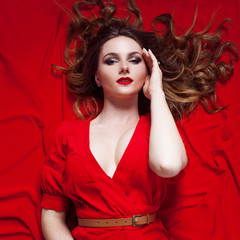 Woman in dress  lies on a red background     