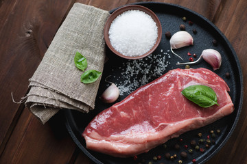 Top view of raw striploin steak with seasonings in a frying pan