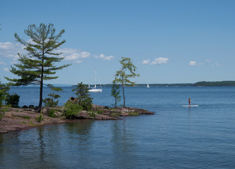  rocky shore with trees  where water sports on lake can be seen: someone paddle boarding and a sailboat  nearby