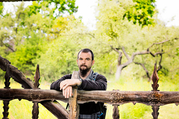 Fototapeta premium Bearded young man leaning on an old carved wooden fence.