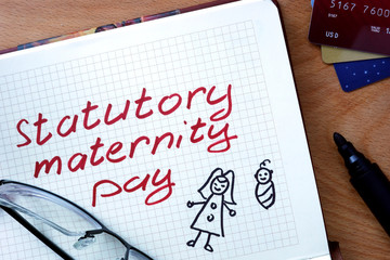 Notepad with statutory maternity pay on office wooden table.